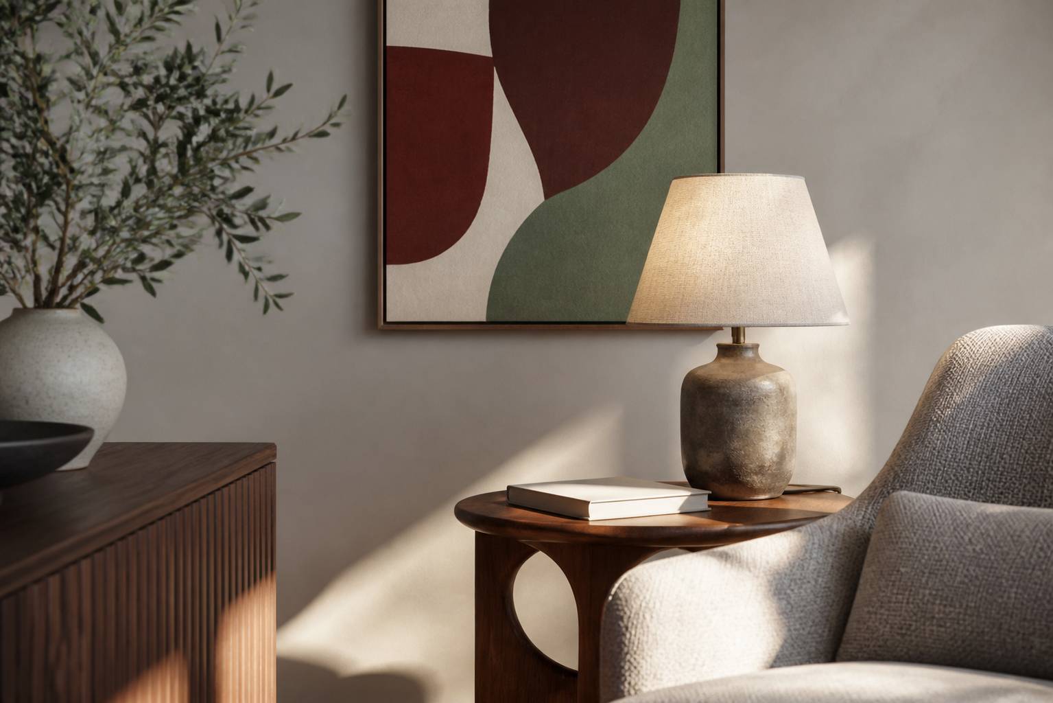 Coin salon avec mur gris clair, cadre aux tons bordeaux, guéridon en bois et lampe chaude